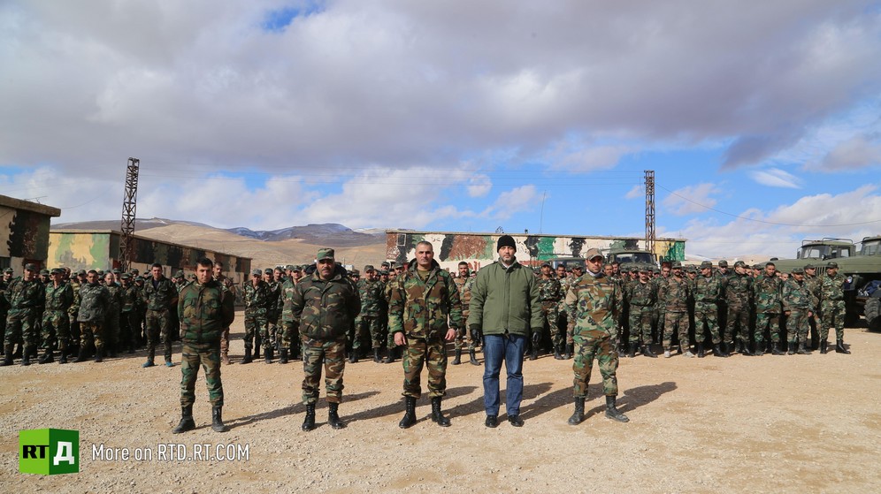 A Syrian army unit made up of amnestied fighters is standing in uniform in front of barracks. Five officers stand to attention in the foreground, under a bright blue sky with large clouds. Taken while filming RTD documentary about Syrian amnestied fighters Amnesty in Wartime. 