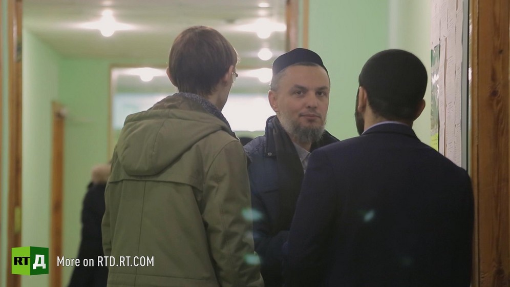 Said Damir Shagaviev wearing a traditional skullcap and a small beard is looking at the camera while talking to two men with their backs to the camera in a corridor in Kazan, Russia. Still taken from RTD's documentary series on Fethullah Gulen, The Gulen Mystery, Episode 2: Gulen's Hizmet Movement.