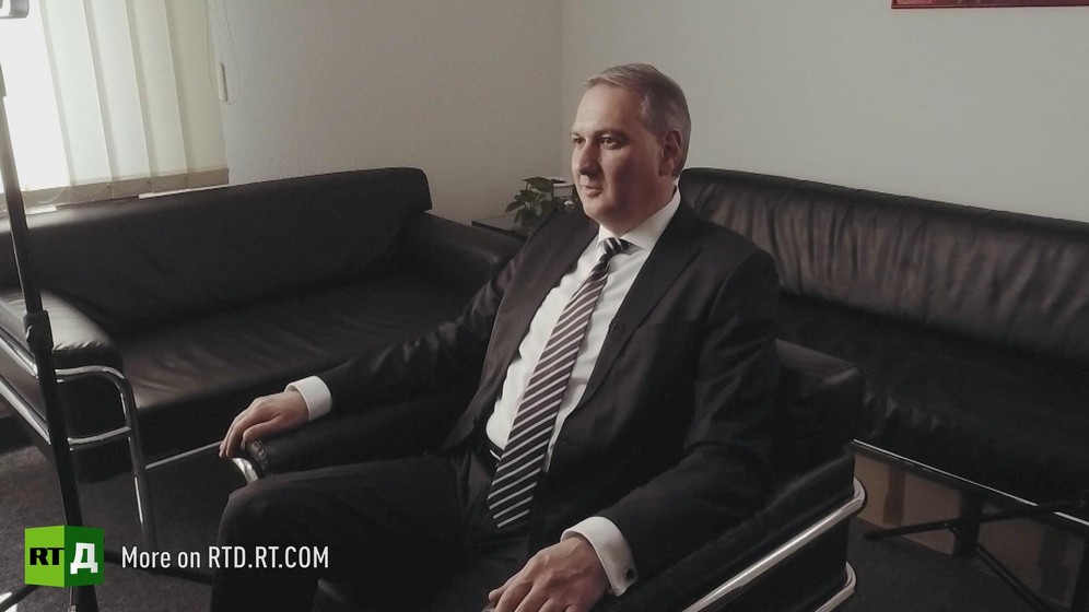 In Germany, entrepreneur Teyfik Ozcan wearing a suit and tie is sitting in a black leather armchair, surrounded by two sofas. Still taken from RTD's documentary series on Fethullah Gulen, The Gulen Mystery, Episode 3: Gulen's Businessmen.