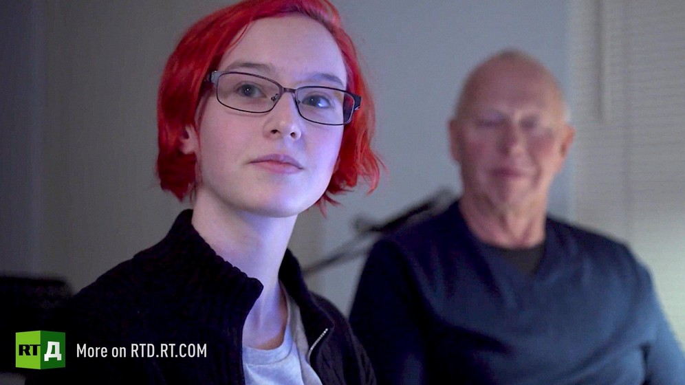 The faces of two childfree by choice generations. A teenage girl with died red hair with her honorary father looking at her in the background. Still taken from RTD documentary Kidless.