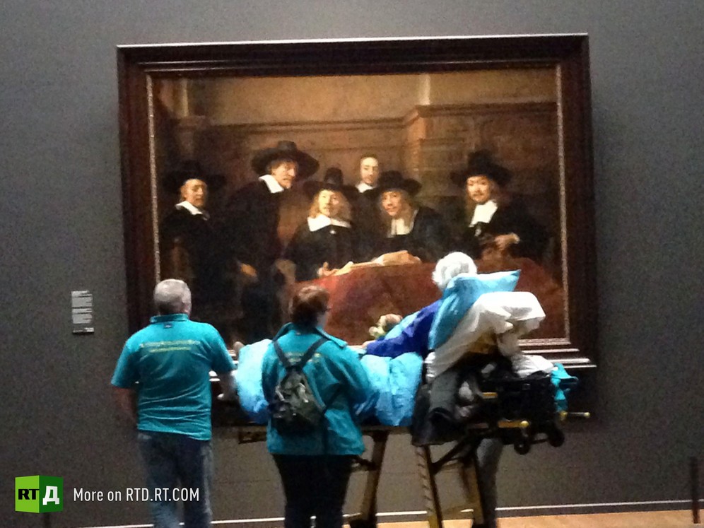 A senior male cancer patient lying on an ambulance stretcher is looking at an Old Master painting, surrounded by volunteers from the Ambulance Wish Foundation during a visit to the Rijksmuseum in Amsterdam, the Netherlands. Still from RTD documentary Last Wishes.