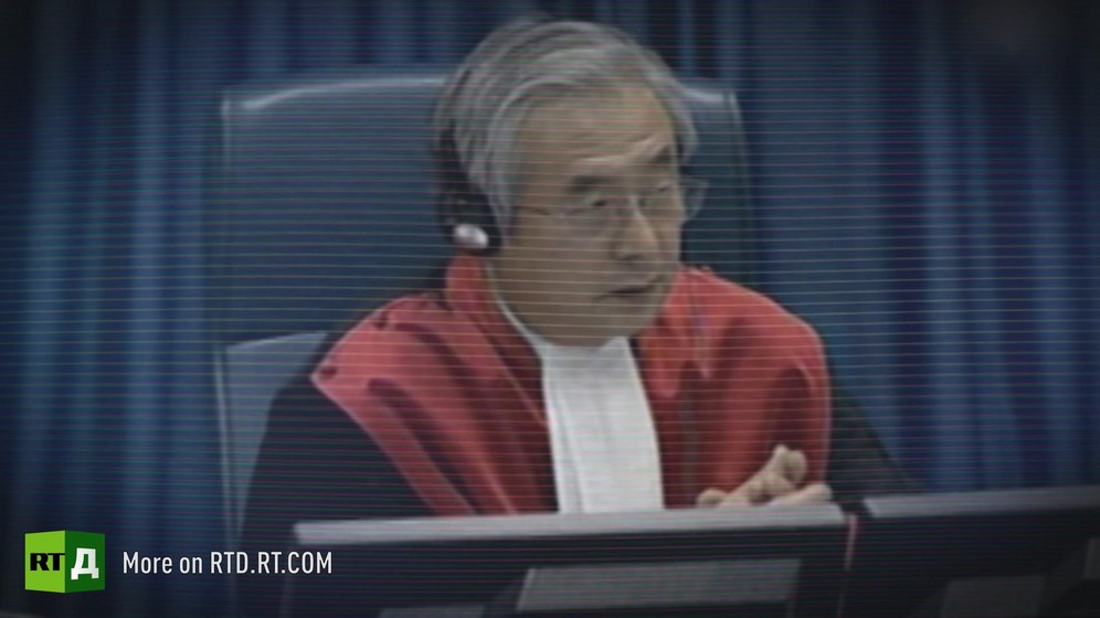 Male judge sitting in a red robe wearing headphones at the International Criminal Tribunal for the Former Yougoslavia. / Archive footage from Republika Srpska Radio and Television.