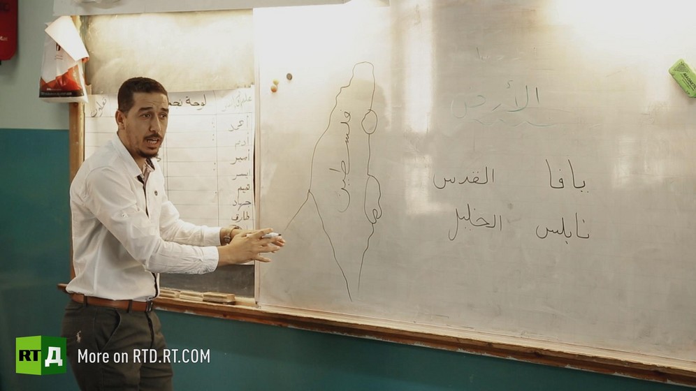 Male Palestinian schoolteacher in front of a map of the territory of greater Palestine on a white board. Still taken from RTD documentary Palestine in Seeking Recognition series.
