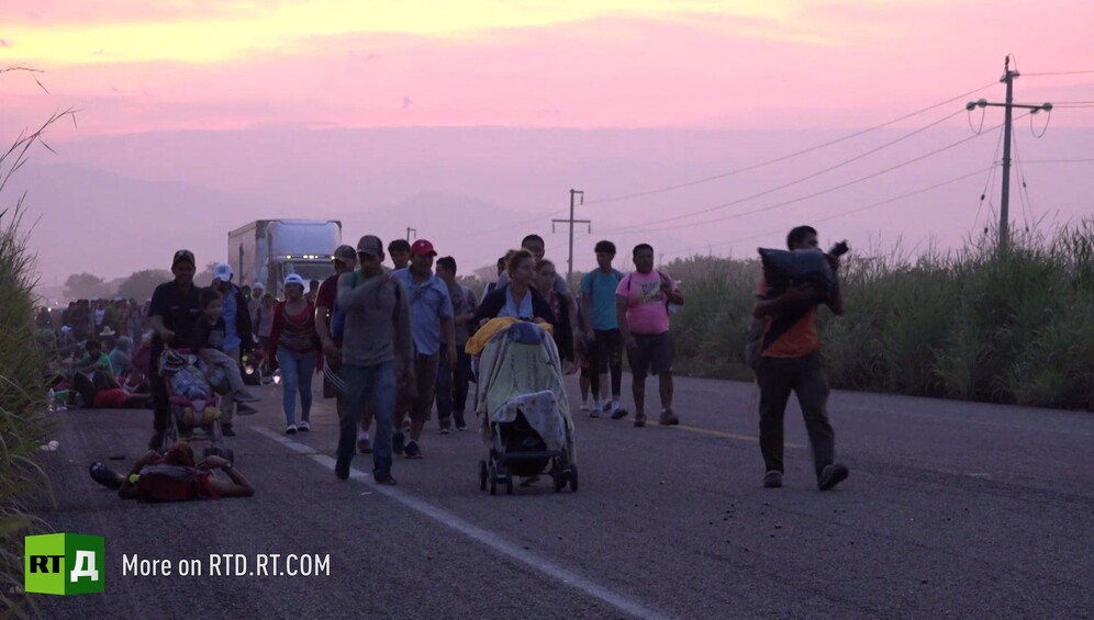 Families in the migrant caravan walking along a road at sunset. Still taken from RTD documentary