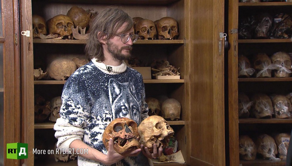 Stanislav Drobyshevsky showing the skulls of a Neanderthal and an Cromagnon in front of a skull cabinet at Moscow State University's anthropology Department