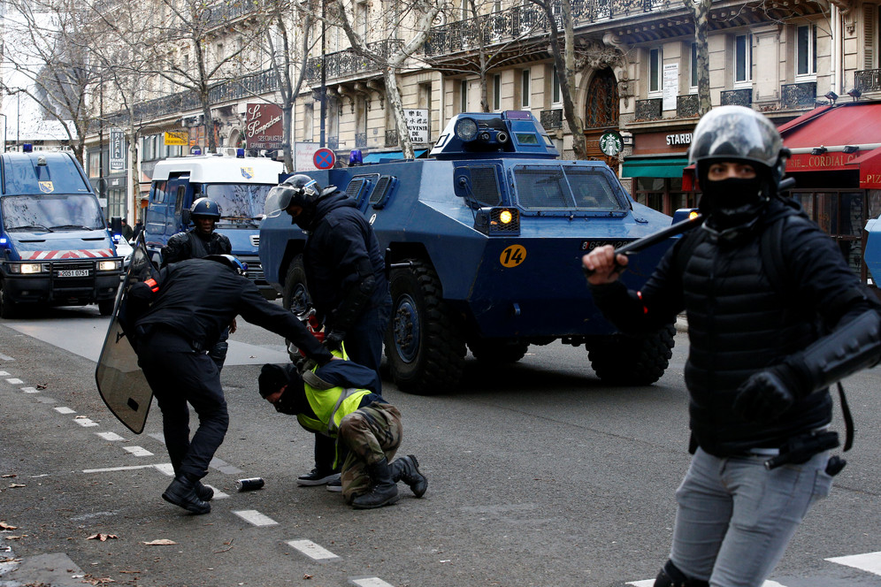 Policeman holds down a Yellow Vest protester with armoured vehicle in the background in Paris, France 