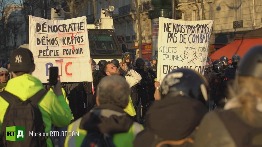 Protesters marching in Toulouse during a Yellow vest protest carrying signs about the RIC and calling Yellow Vests and police to unite. Still taken from RTD 's documentary, Yellow Vest Fever.