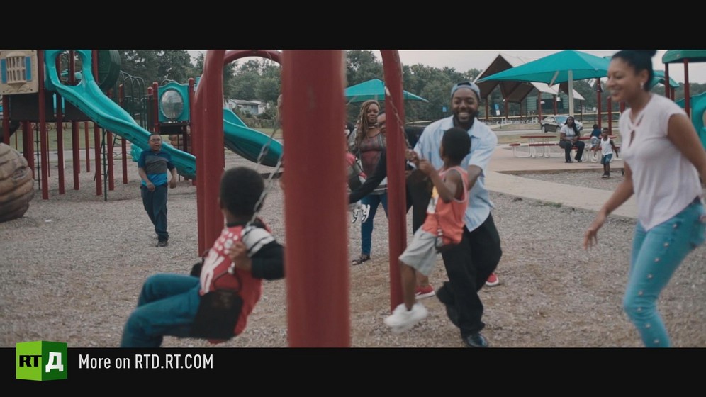 African American families playing on swings at playground. Still taken from RTD documentary, Black Lives 10: Trap.