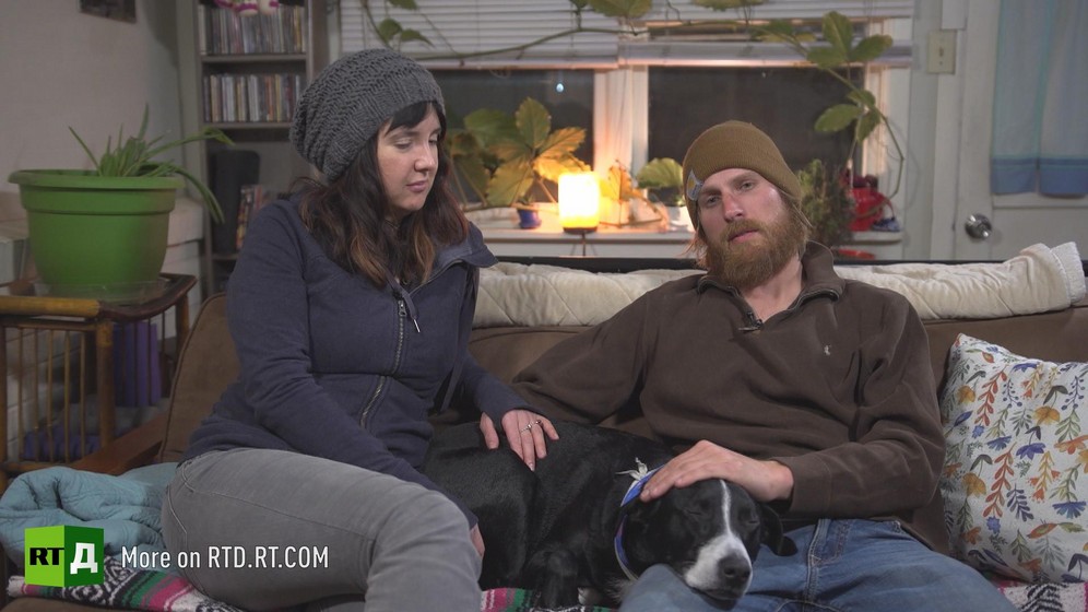 A childfree husband and wife look at each other while sitting on a sofa with a dog in the middle. Still taken from RTD documentary Kidless.